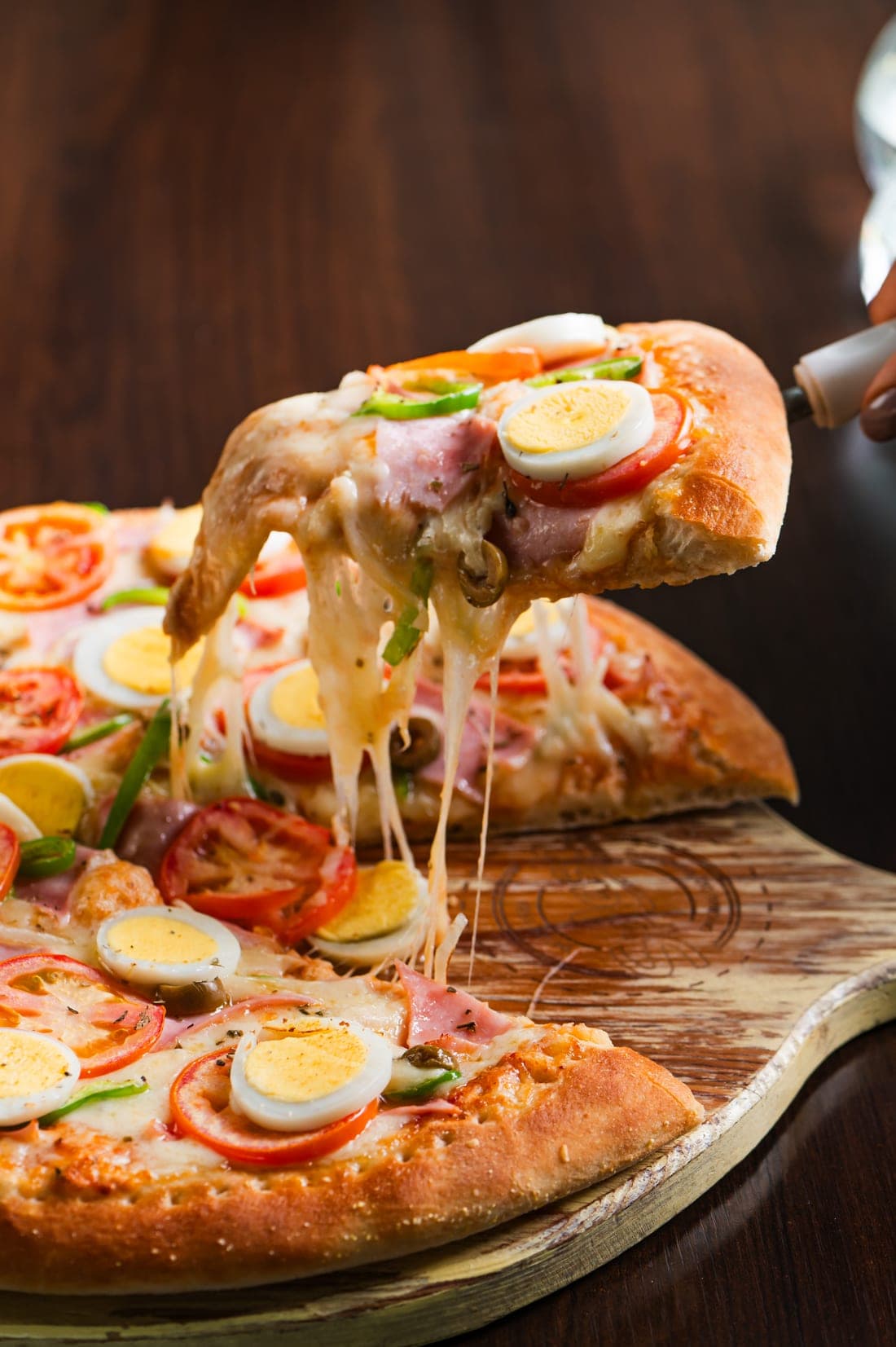 Fatia de pizza com presunto, ovo e tomate, com queijo esticando