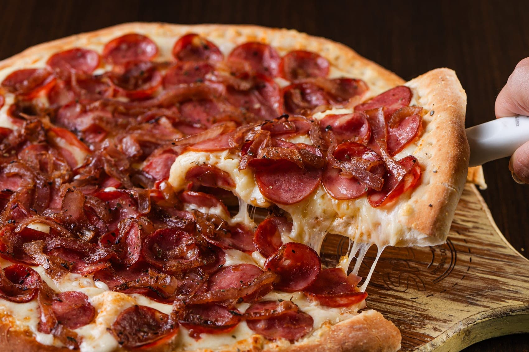 Pizza de calabresa e bacon com queijo derretendo, servida na pá